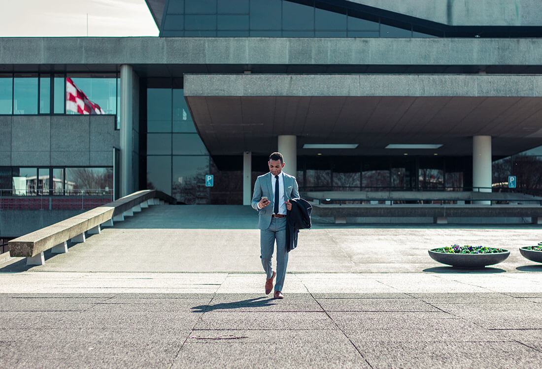 Photo of man in a suit walking and using his phone